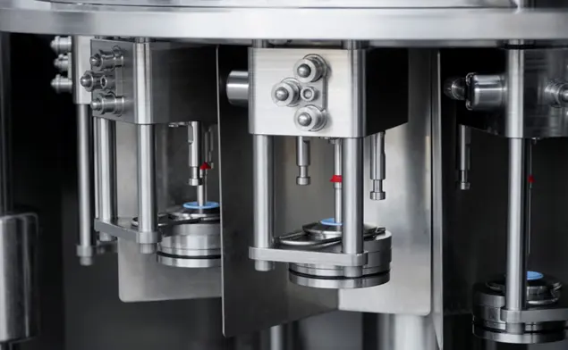 Close-up of a stainless steel industrial filling machine with vertical pistons and clamps, showing precision hardware.