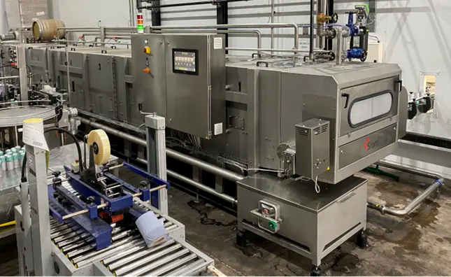 Industrial processing equipment: large stainless steel machine with control panel and pipes in a factory setting.